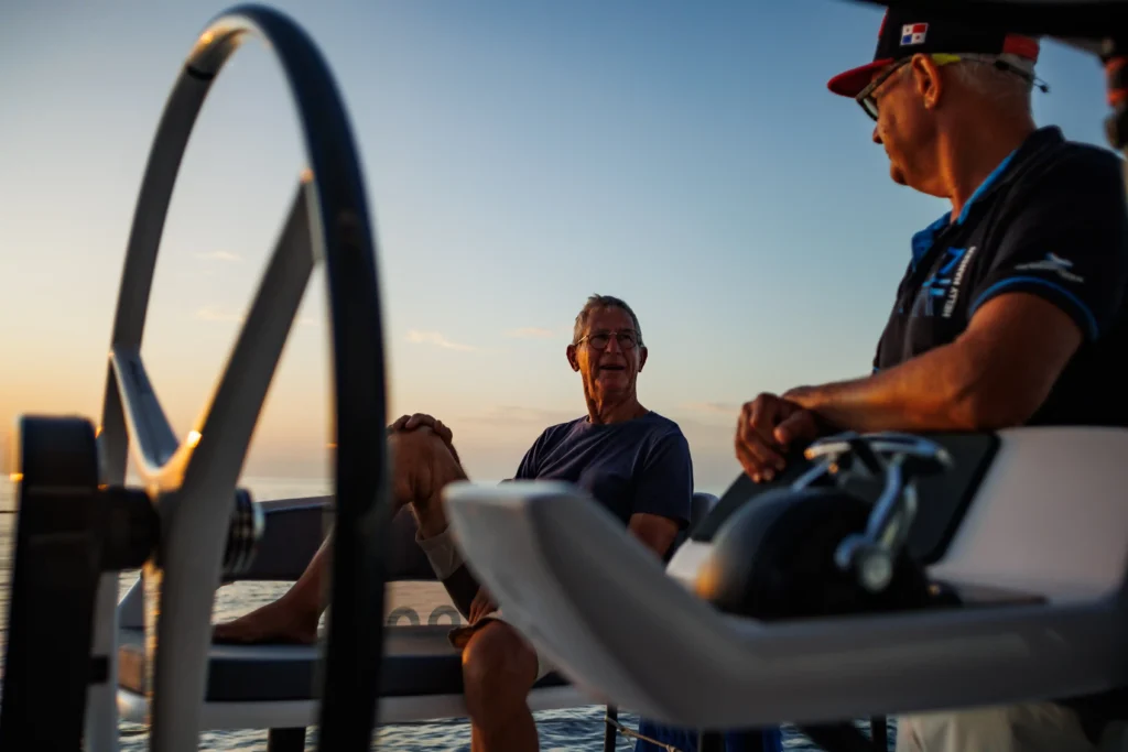 Deux marins discutent à la barre d’un voilier au coucher du soleil pendant leur tour de l’Atlantique